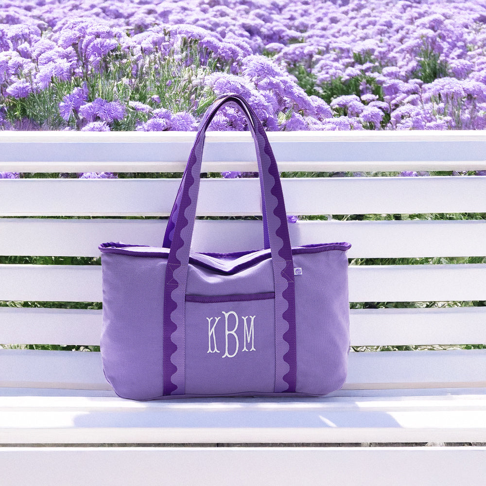 Purple tote bag with initials 'KBM' on a white bench in front of lavender flowers