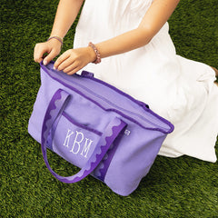 Person holding a purple bag with 'KBM' monogram on grass