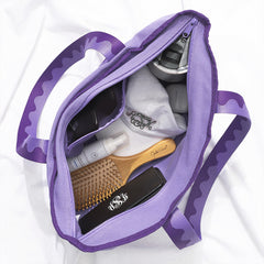 Purple tote bag with hairbrush, bottle, and cap on a white background