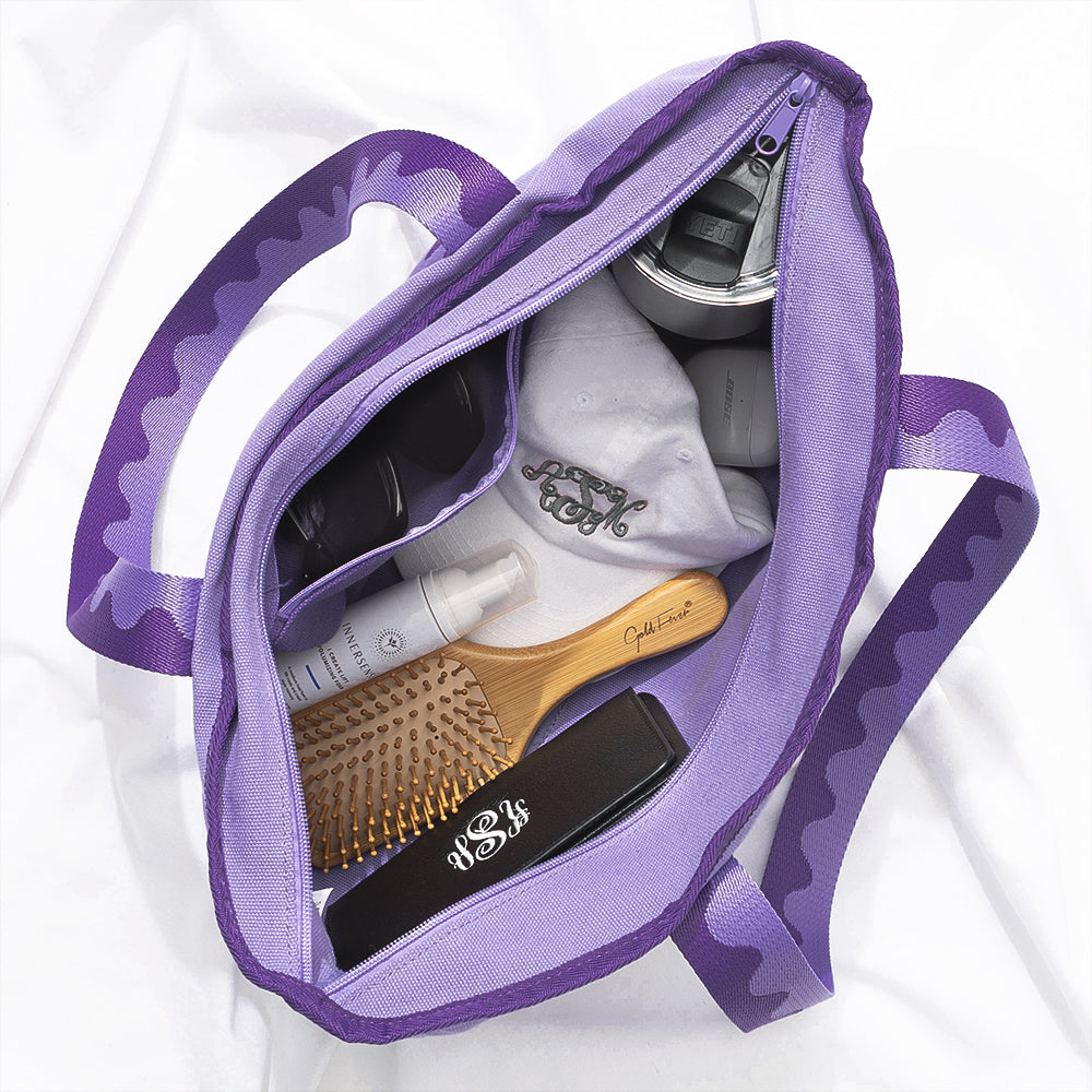 Purple tote bag with hairbrush, bottle, and cap on a white background