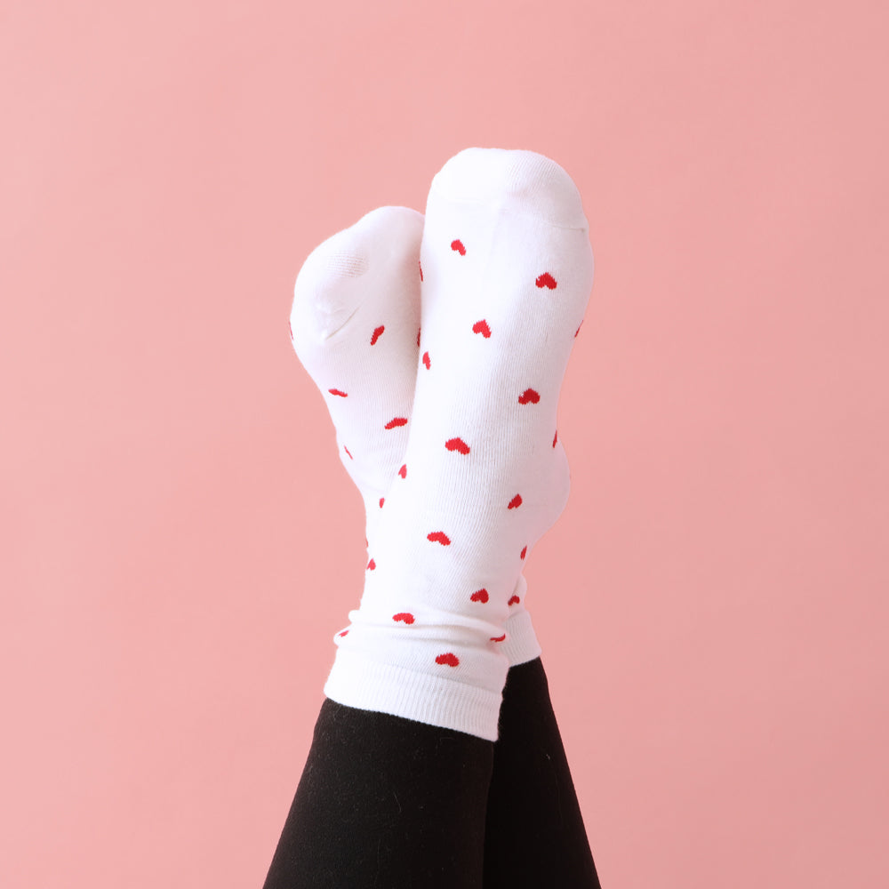 heart socks on crossed ankles on front of pink paper