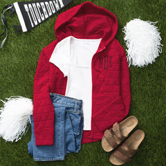 red quilted hoodie flatlay with pom poms and flag