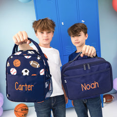 sports balls lunchbox and navy lunchbox held by boys