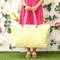 Person holding a yellow striped tote bag with pink handles against a floral background