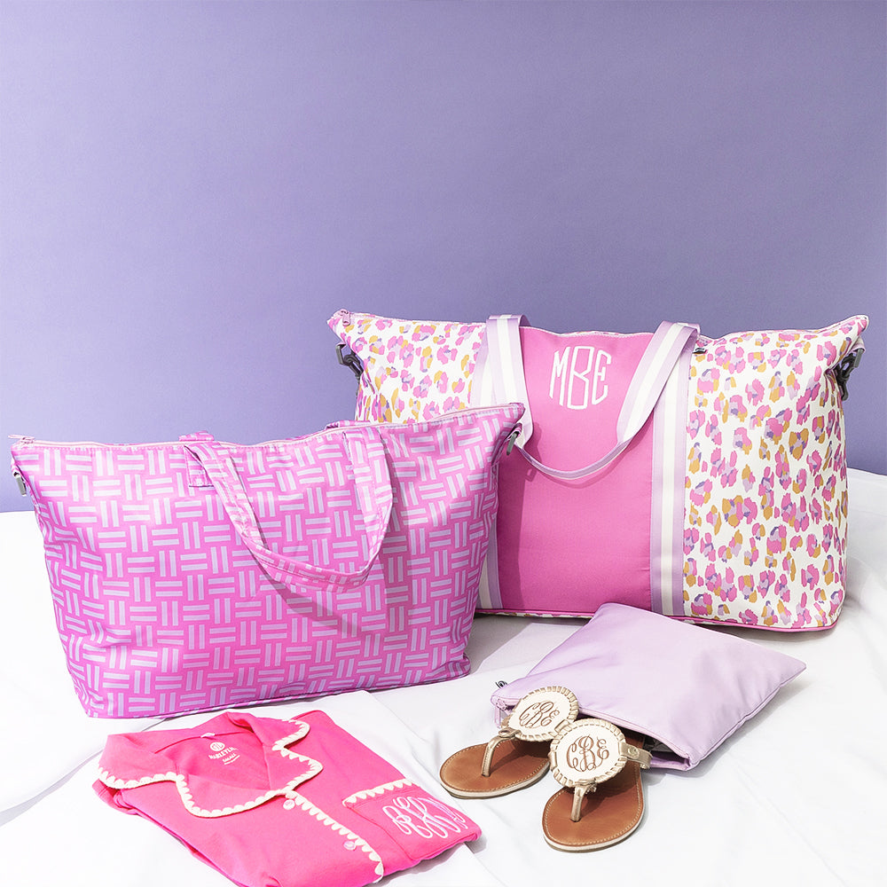 Pink bags and accessories with monogram on a white surface against a purple background