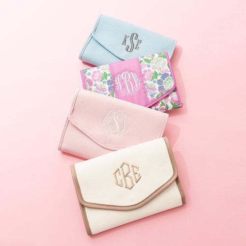 Four monogrammed jewelry organizer bags on a pink background
