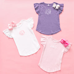 Three children's shirts with ruffled sleeves and bows on a pink background