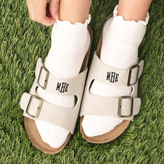 Tan monogrammed sandals with buckles worn on grass