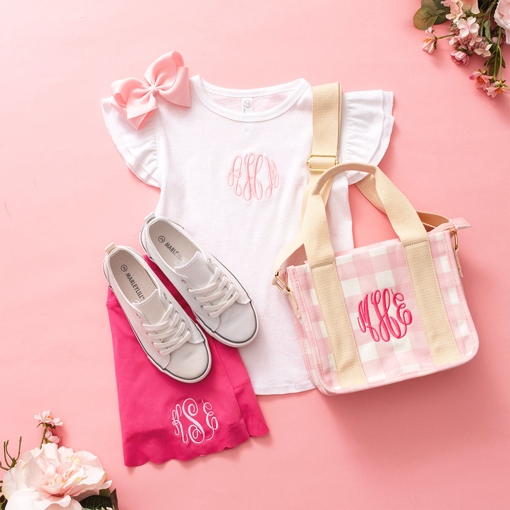 White shirt with pink bow, pink shorts, white sneakers, and a pink and gold bag on a pink background.