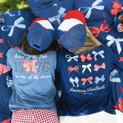 women laying on picnic blanket wearing light navy and bows america t-shirt