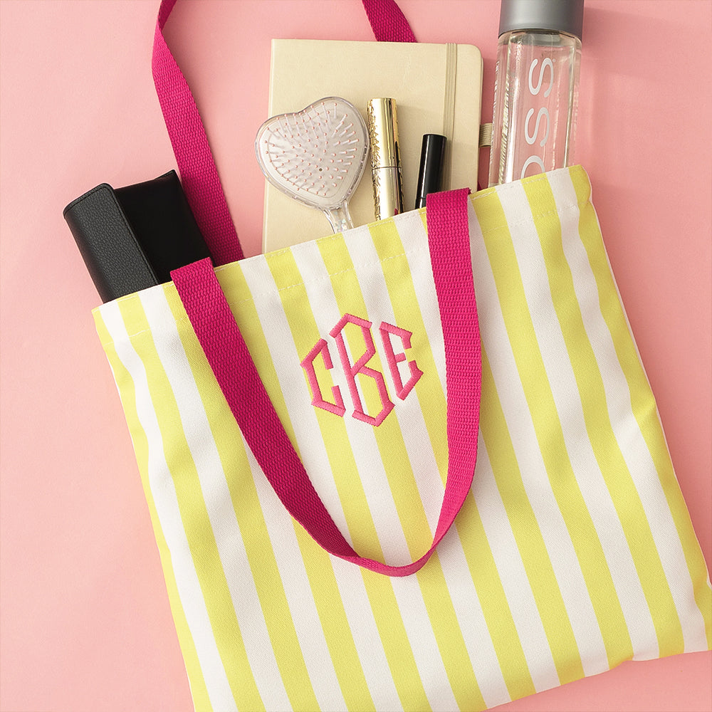 yellow striped tote bag with items spilling out on pink background